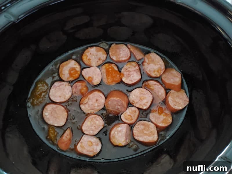 Sliced kielbasa simmering in a rich, glossy sauce in a slow cooker bowl, ready to be served as an appetizer.