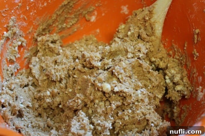 A vibrant orange bowl filled with the initial mixture of peanut butter, powdered sugar, and melted butter, before the cereal is added.
