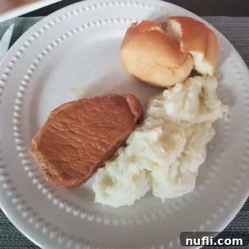 white plate with a roll, potatoes, and pork loin