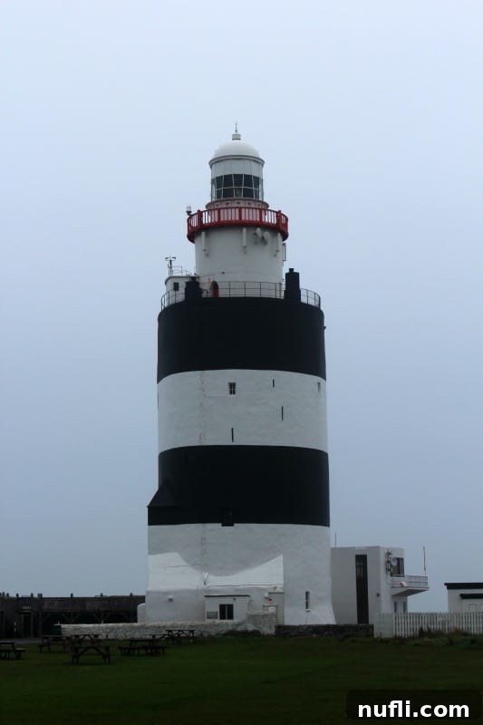 The iconic Hook Head Lighthouse with its distinctive black and white stripes reaching towards the sky, set against a dramatic coastal backdrop.