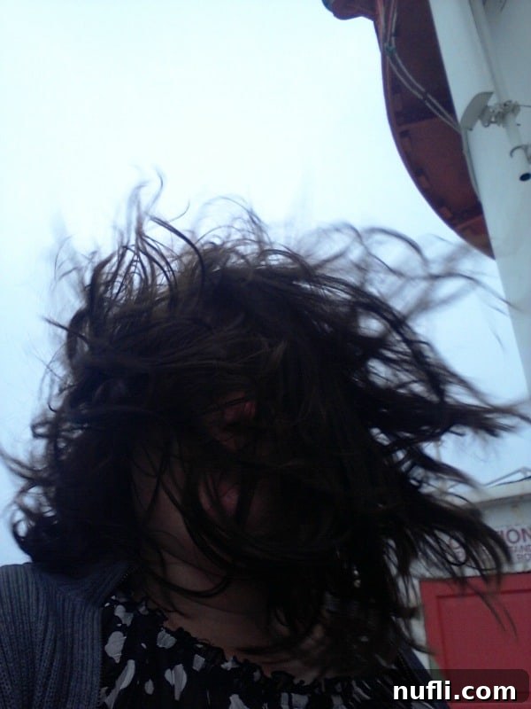 A person named Tammilee with her hair blowing wildly in all directions on the windy balcony of Hook Head Lighthouse, illustrating the strong coastal winds.