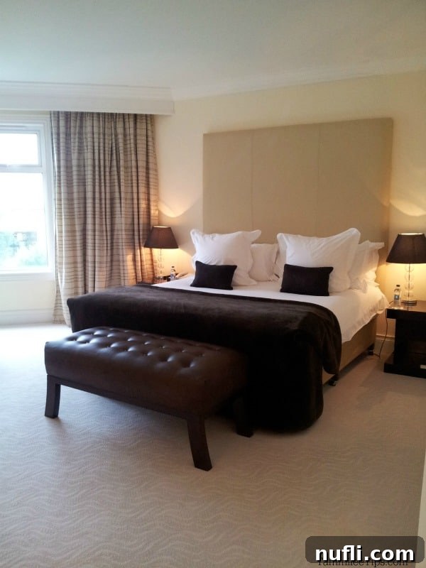 Comfortable hotel room featuring a bed, a stylish leather footstool, and elegant nightstands.