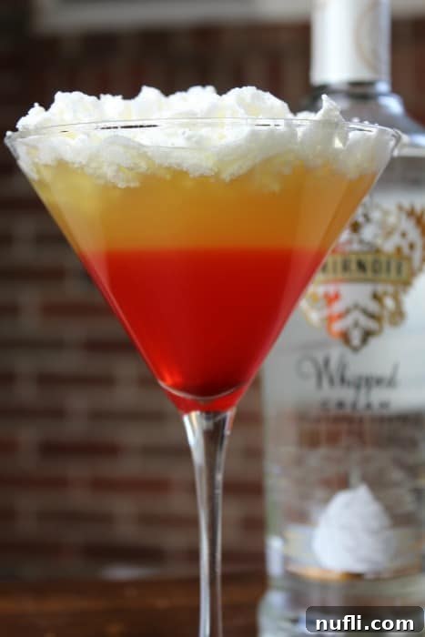 Candy corn cocktail in a martini glass with whipped cream vodka behind it