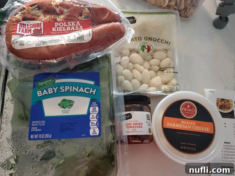 Key ingredients for Smoked Sausage Gnocchi: sliced kielbasa, vibrant baby spinach, pillowy potato gnocchi, tangy sun-dried tomatoes, and a generous sprinkle of Parmesan cheese, laid out on a clean surface.