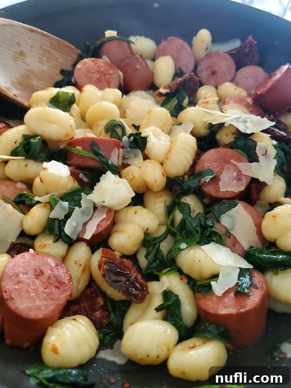 A rustic cast-iron skillet filled with tender gnocchi, savory kielbasa, sweet sun-dried tomatoes, and rich Parmesan cheese, ready to be served with a wooden spoon.