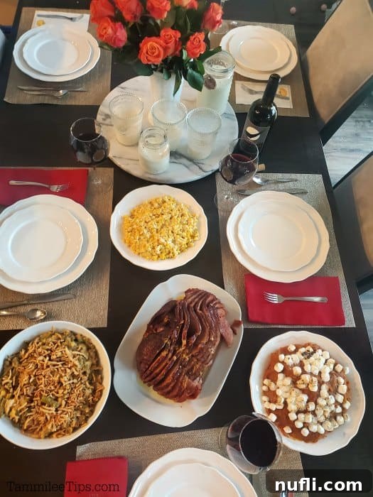 A festive dining room table set for a holiday meal, featuring candles, roses, white plates, a roasted ham, green bean casserole, corn, and a Crockpot Sweet Potato Casserole.