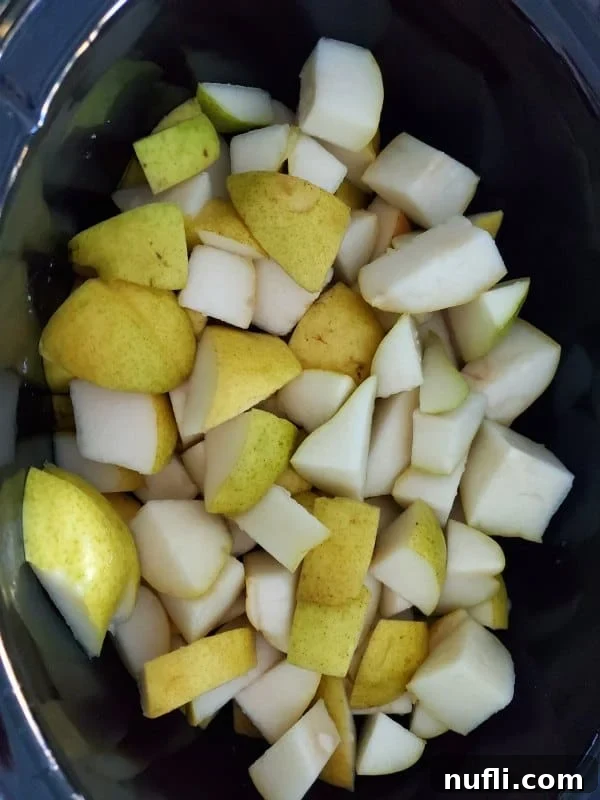 Easy Homemade Slow Cooker Pear Butter 3 pears cut into pieces in a dark slow cooker bowl