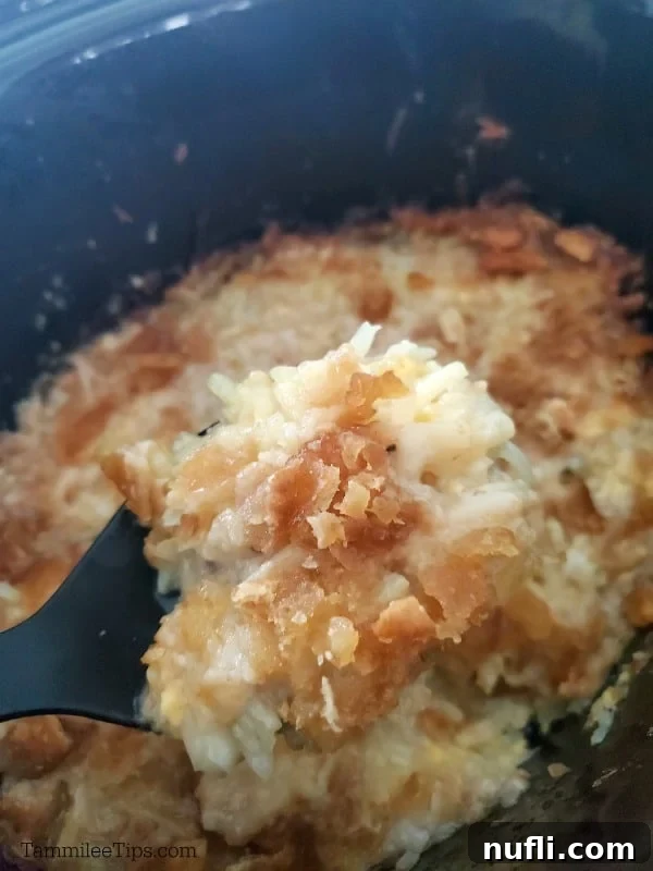 Creamy Slow Cooker Hashbrown Casserole 6 Close-up of golden, cheesy hashbrowns being lifted from the slow cooker with a dark spoon, showing their creamy texture.