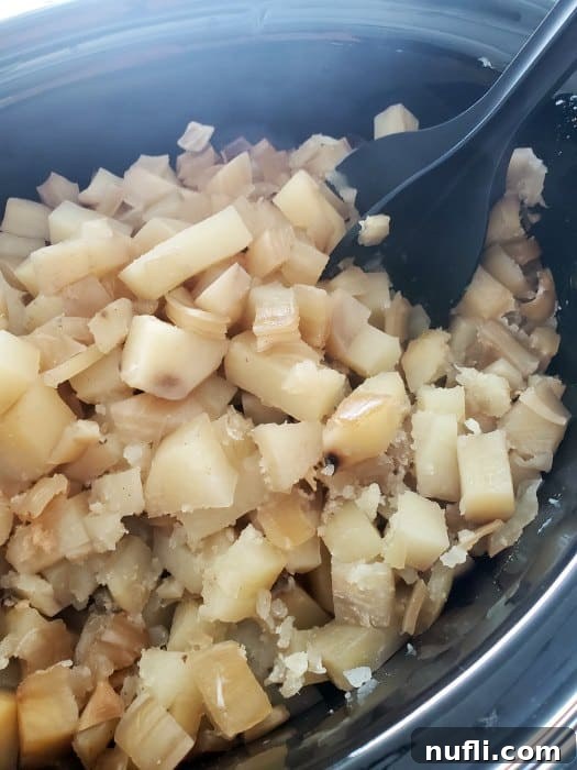 A mix-and-chop tool breaking up tender potato pieces directly in a crockpot, creating a creamy texture.