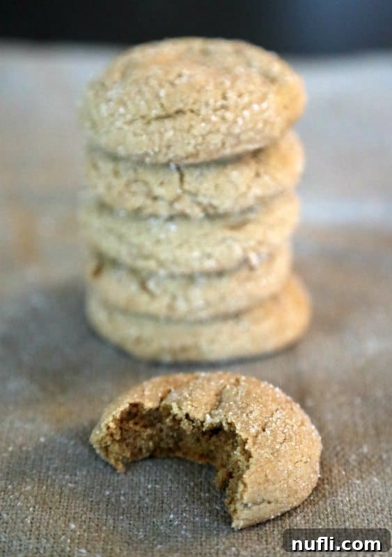 Stack of soft molasses cookies on burlap with one cookie showing a bite taken out, emphasizing its soft, chewy interior.