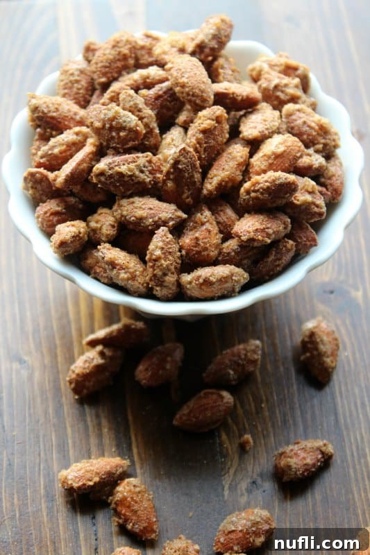 A white bowl brimming with golden-brown sugar and spice coated almonds, ready to be enjoyed or gifted.