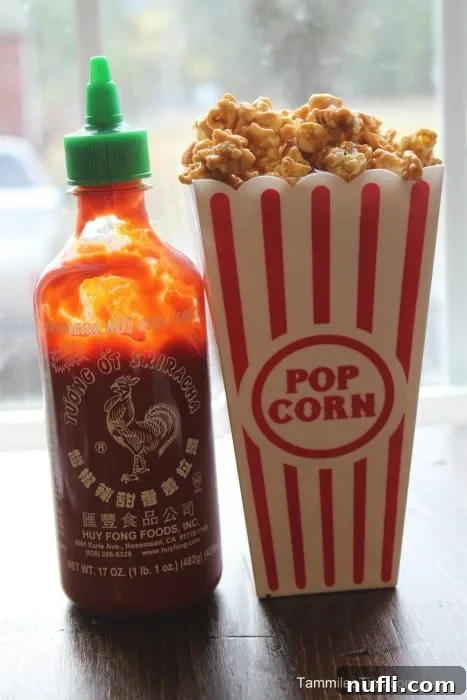 Bottle of Sriracha next to a container of popcorn