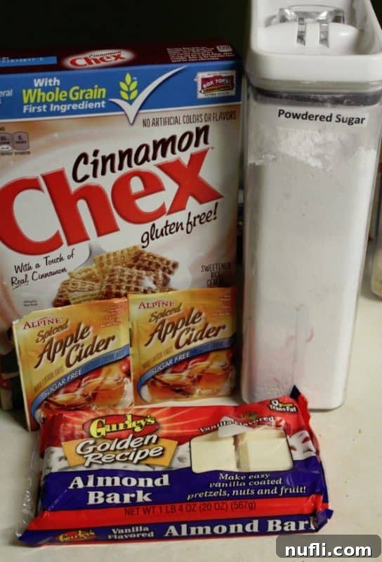 Essential ingredients for Apple Cider Muddy Buddies: Cinnamon Chex cereal, powdered sugar, apple cider mix, and vanilla almond bark, neatly arranged on a kitchen counter.
