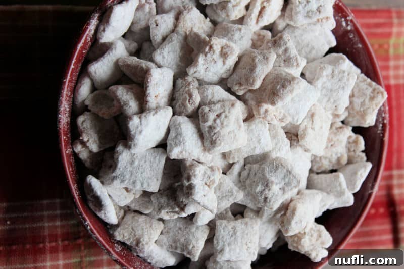 A deep red bowl brimming with Apple Cider Muddy Buddies, ready to be enjoyed.