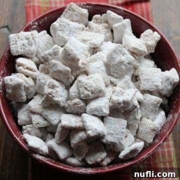 Apple Cider Muddy Buddies in a burgundy bowl on a wood board
