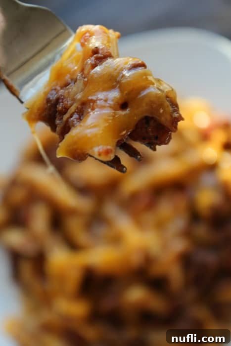 Fork lifting a spoonful of cheesy pasta beef casserole from a large serving bowl