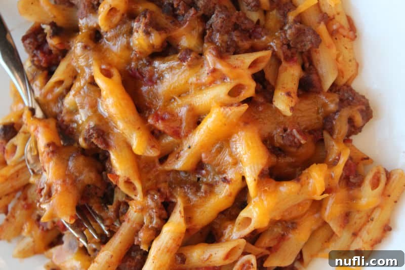 cheesy pasta beef casserole on a white plate with a fork, ready to eat