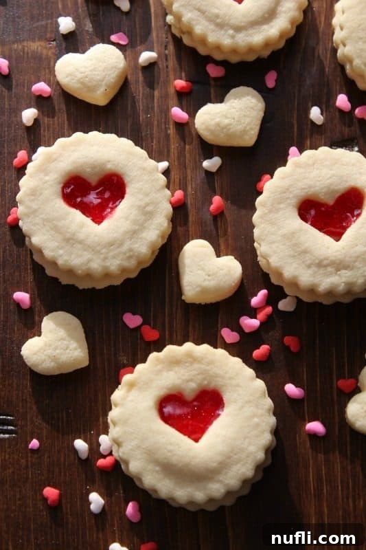 Linzer cookies with red heart cutouts, filled with red icing and sprinkled with more tiny red hearts.