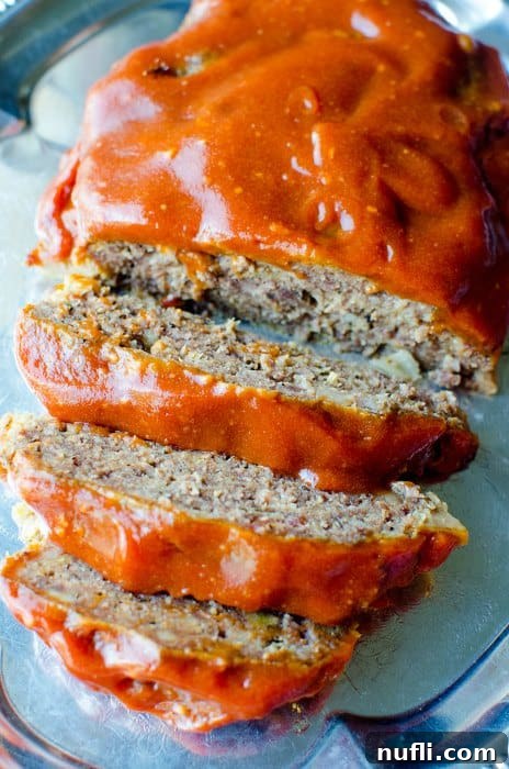 Effortless Slow Cooker Meatloaf 3 Slices of slow cooker meatloaf drizzled with a rich, tangy ketchup glaze on a reflective silver platter.