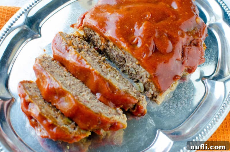 Effortless Slow Cooker Meatloaf 4 Close-up of a perfectly sliced crockpot meatloaf, glazed and ready to be served, on a silver platter.