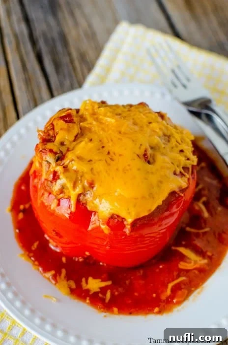 Melted cheddar cheese on a crockpot stuffed pepper in a white bowl with a yellow napkin, against a brown wood background