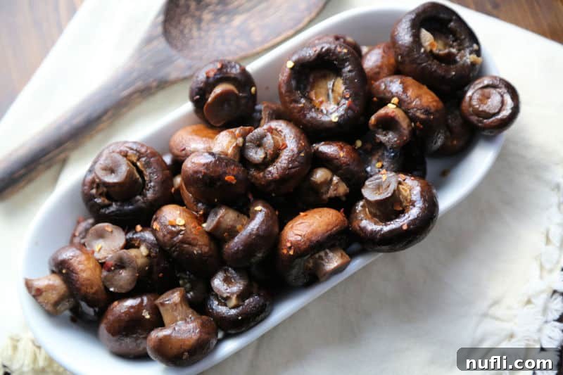 Easy Slow Cooker Mushrooms 4 mushrooms in crock pot spread in a white bowl with a wooden spoon.