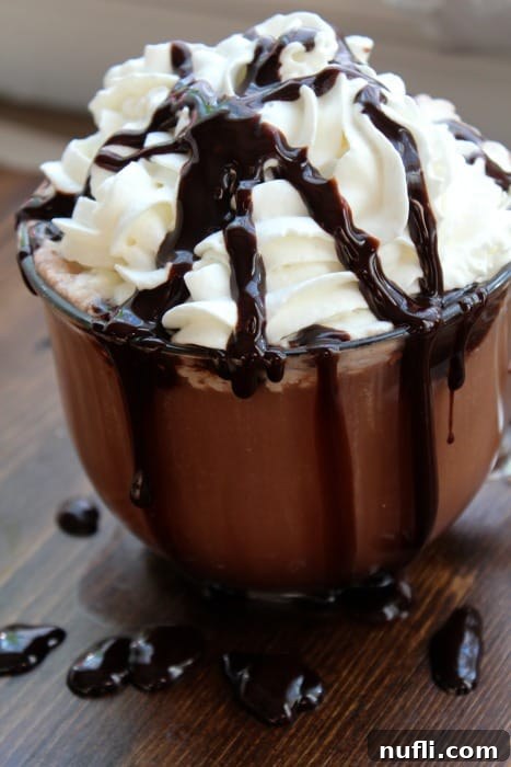 Cozy Slow Cooker Hot Chocolate 7 Hot chocolate in a glass mug garnished with a heaping pile of whipped cream and chocolate syrup