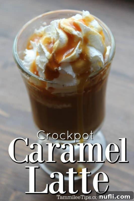 A perfectly frothed Crockpot caramel latte in a clear glass mug, topped generously with whipped cream and a drizzle of golden caramel sauce, sitting on a rustic wooden surface next to a warm blanket.