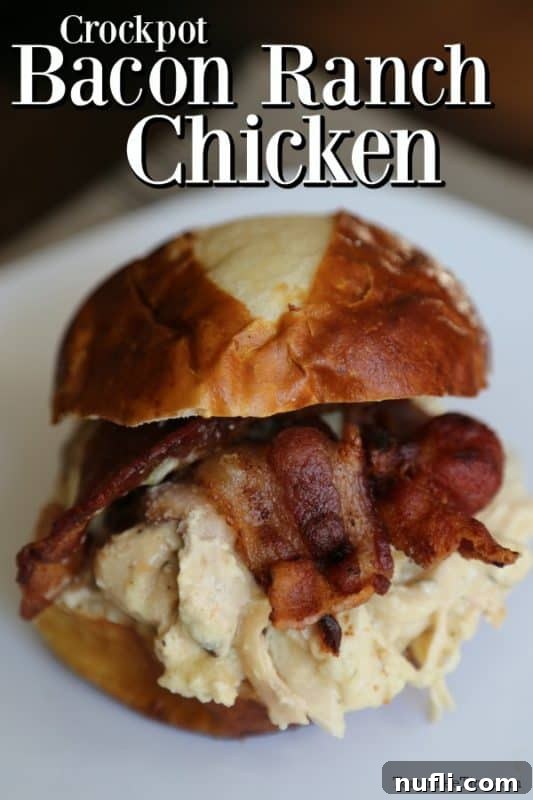 Easy Slow Cooker Bacon Ranch Chicken 2 Tender Crockpot Bacon Ranch Chicken shredded and served over a white plate with a delicious sandwich on a bun beside it, garnished with fresh herbs.