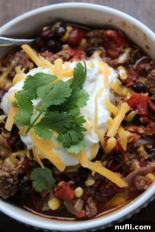 Close-up of a white bowl filled with spicy taco soup, adorned with a swirl of sour cream and a sprinkle of cheese