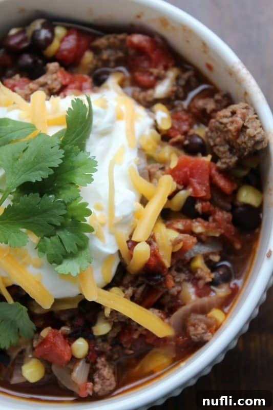 A top-down view of taco soup in a white bowl, generously topped with sour cream and shredded cheese