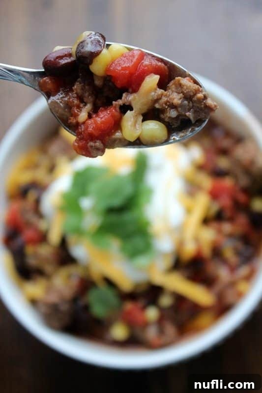 A spoon lifting a portion of spicy taco soup, showing the rich texture and ingredients, above a white bowl