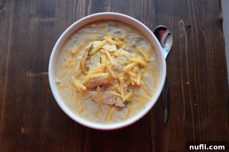 A white bowl of creamy Crock Pot Cheeseburger Soup with a sprinkle of shredded cheese and a silver spoon resting on the side, highlighting its inviting texture.