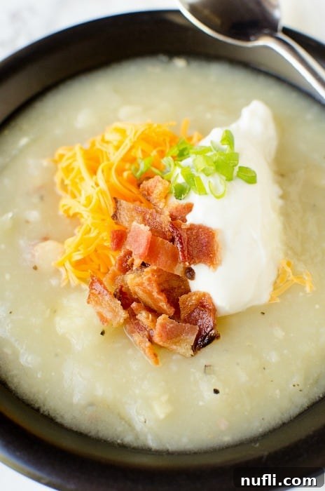 Creamy potato soup with bacon, sour cream, and cheese on top in a dark bowl