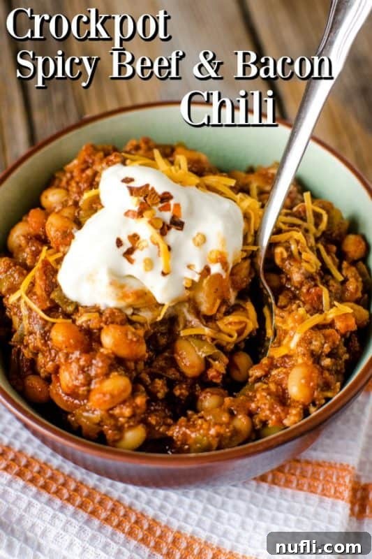 Hearty Crock Pot Spicy Bacon and Beef Chili 2 Hearty Crock Pot Spicy Bacon and Beef Chili, garnished with a dollop of sour cream and a spoon, ready to be enjoyed.
