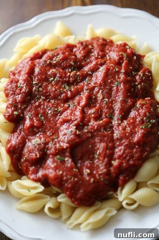 A white plate with perfectly coated pasta shells in rich marinara sauce, ready to be enjoyed.