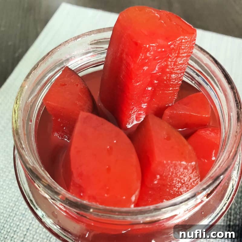 Effortless Entertaining: Simple Finger Foods for Any Party 13 Vibrantly colored Cherry Kool-Aid Pickles in a glass jar, with one sticking out, showcasing their unusual and fun appeal.