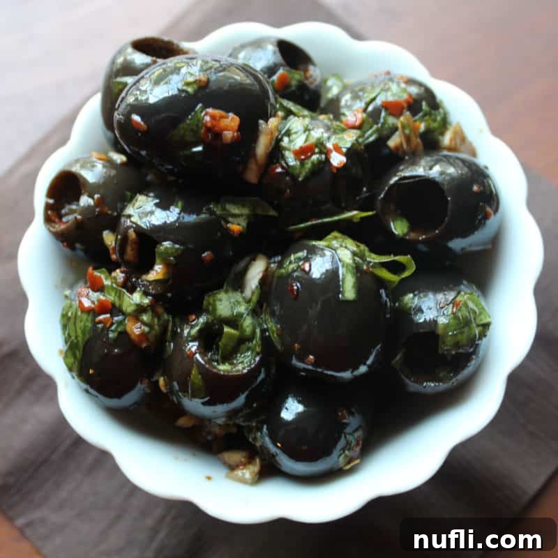 Effortless Entertaining: Simple Finger Foods for Any Party 15 Glossy Marinated Olives in a white bowl, glistening with herbs and oil, perfect for an elegant appetizer spread.