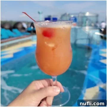 pink orange cocktail in a hurricane glass with a cherry in front of a pool
