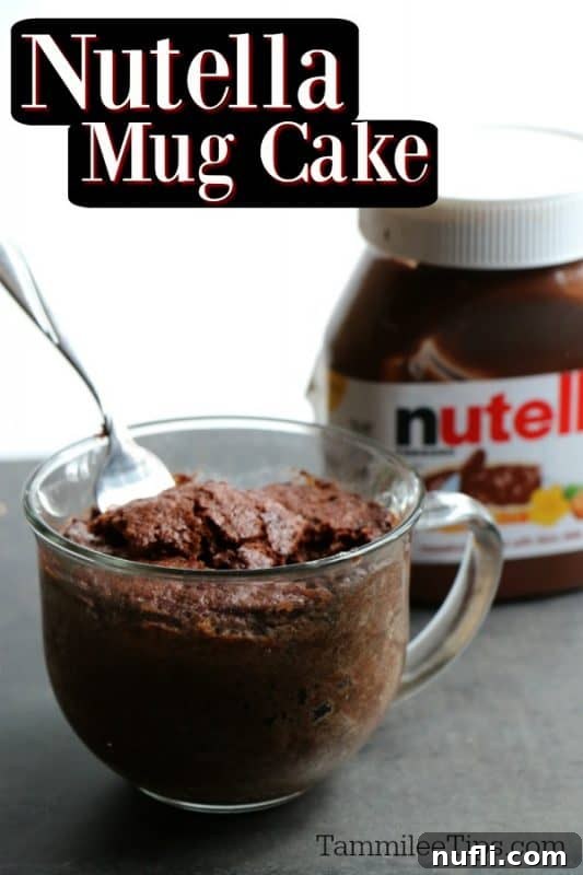 A perfectly baked Nutella Mug Cake in a clear glass mug, with a jar of Nutella in the background, inviting a delightful experience.