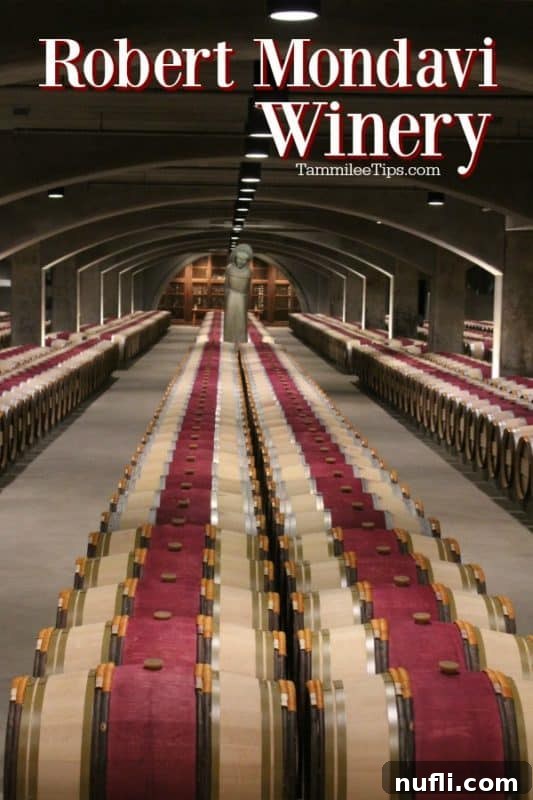 Robert Mondavi Winery's historic mission-style architecture overlooks rows of vibrant green vineyards under a clear Napa sky, with oak barrels subtly featured, symbolizing tradition and quality.