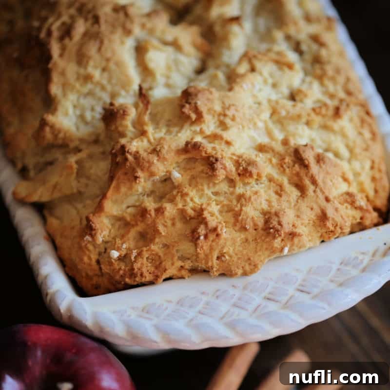 Apple Beer Bread in a white baking dish next to an apple and cinnamon sticks