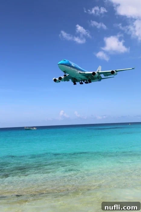 Plane landing over the turquoise water at Maho Beach, St. Maarten, with spectators on the beach