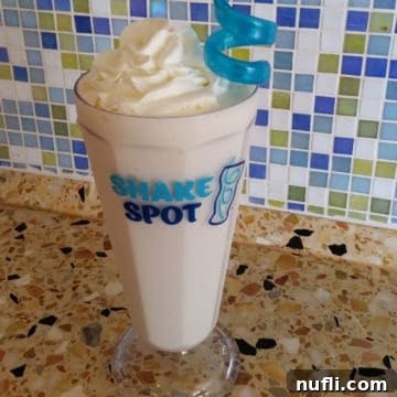 Shake spot glass with a bourbon milkshake with whipped cream garnish and a blue straw