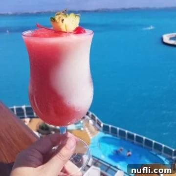 Miami Vice Cocktail in a hurricane glass with pineapple and cherry garnish with the tropical ocean in the background