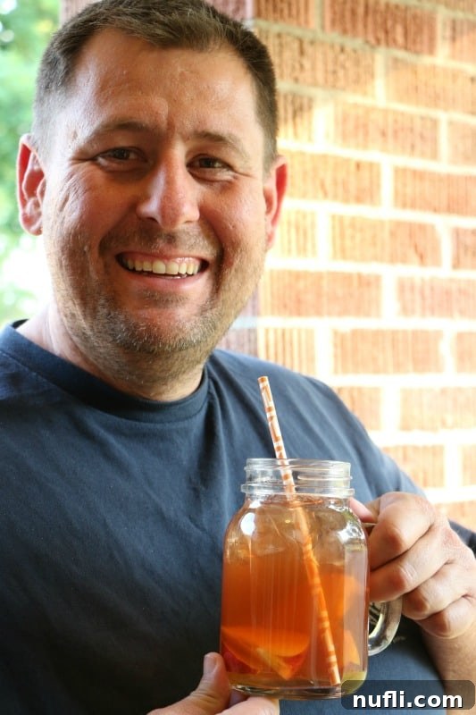 A man smiling while holding a glass of iced peach tea, a perfect summer drink.