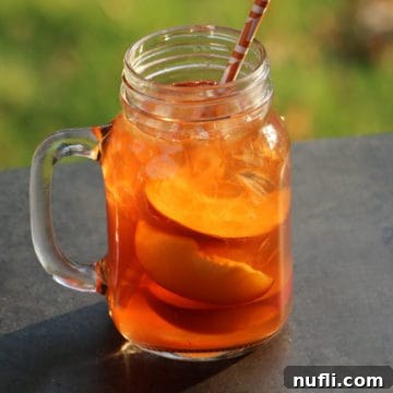 Peach Iced Tea Cocktail in a mason jar glass with sliced peaches and a paper straw
