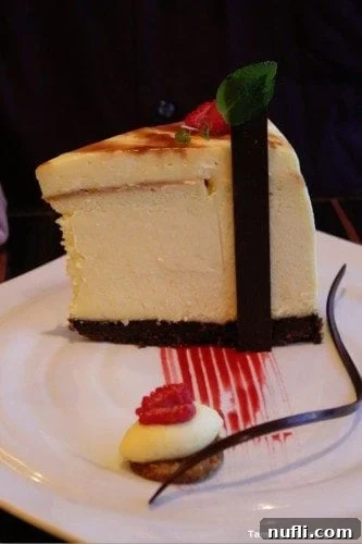 Carnival Breeze Fahrenheit 555 Steakhouse Cheesecake on a white plate with raspberry sauce, a luxurious dessert option