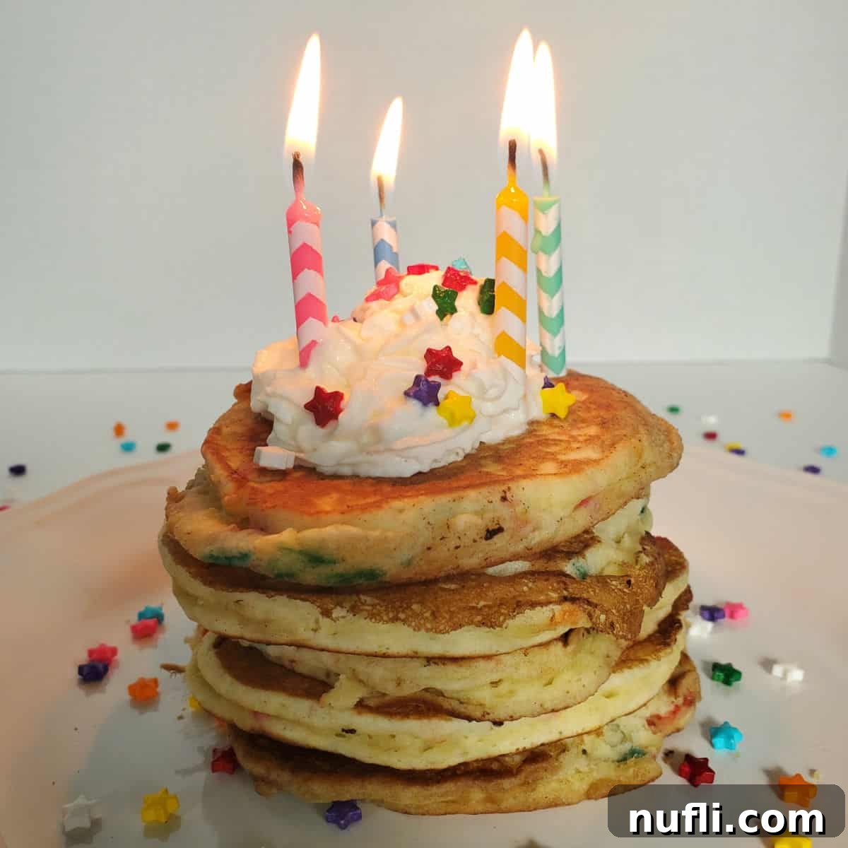 Stack of Funfetti Cake Mix Pancakes on a white plate with lit birthday candles, whipped cream, and sprinkles.