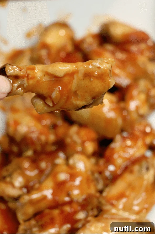 Honey Sriracha coated chicken wing held above a slow cooker, showcasing the sticky, glossy glaze.